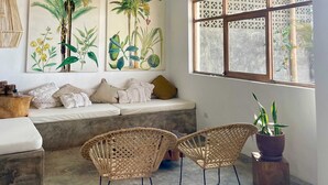 A room with a bamboo ceiling, a large botanical painting, wicker chairs, a cushioned bench, and a window with a lattice design. - HOP MAR Surfea las Mejores Olas de Puemape (Puémape)
