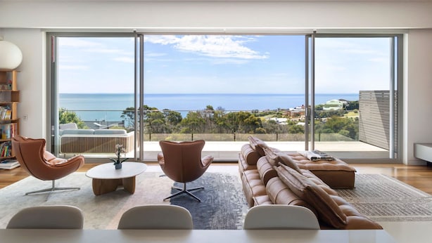 A modern living room with a large sliding glass door leading to a balcony with a sea view.
