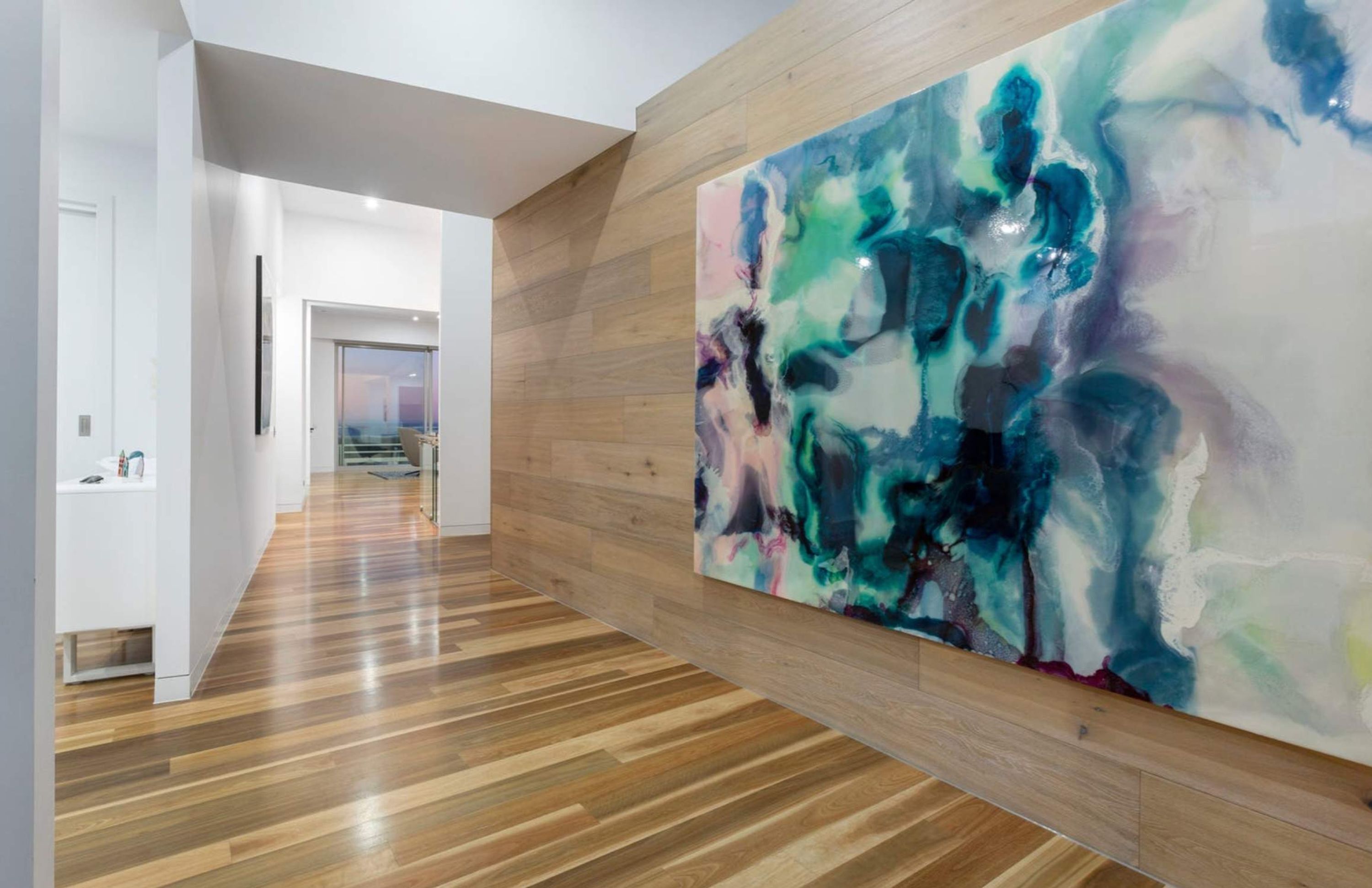 Un couloir doté d’un plancher en bois et orné d’un grand tableau abstrait au mur.