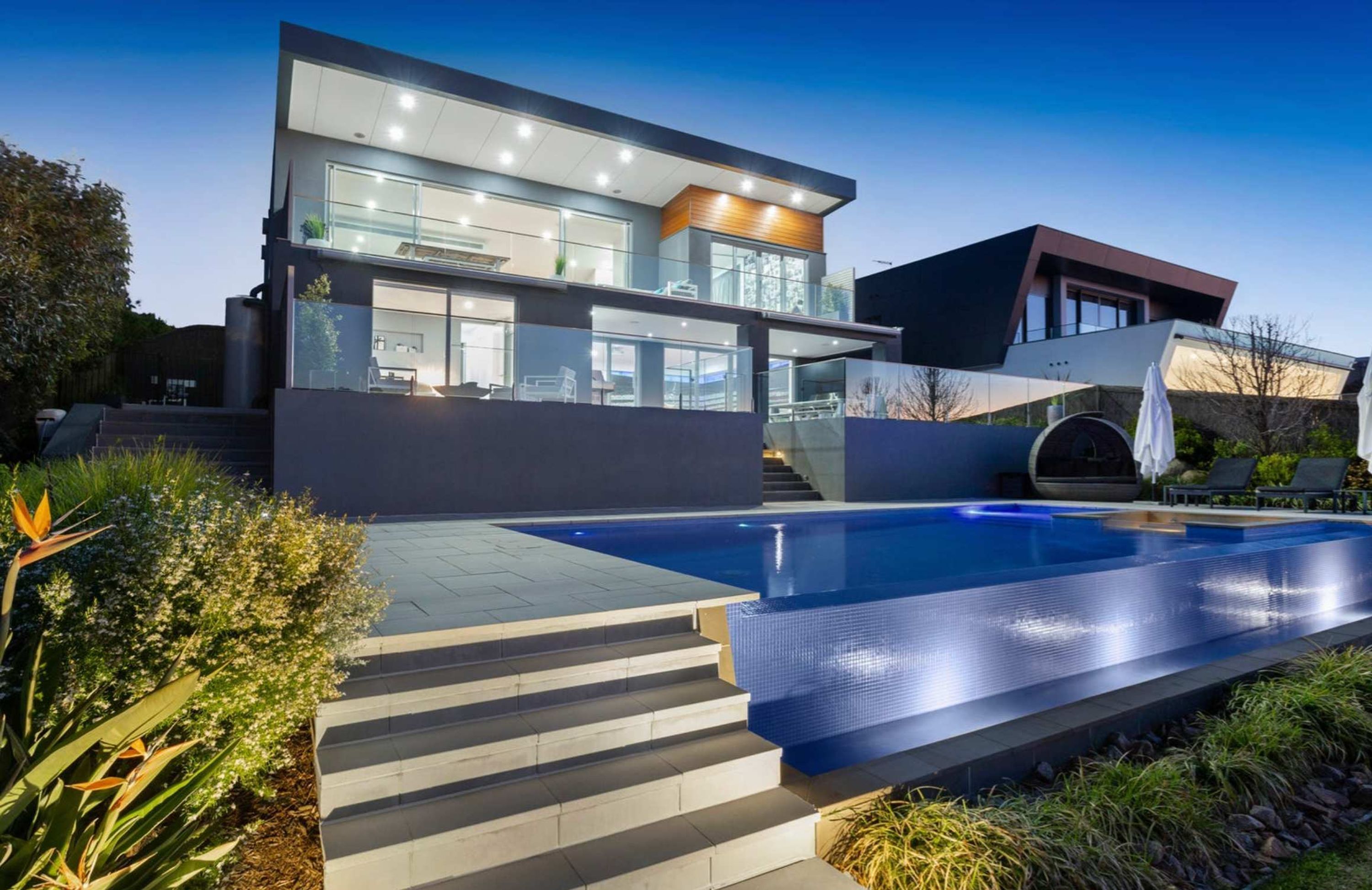 A modern two-story house with a swimming pool, outdoor seating, and a well-maintained garden.