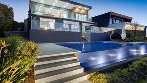 A modern two-story house with a swimming pool, outdoor seating, and a well-maintained garden.