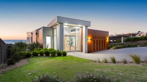 A modern house with a glass entrance, a wooden exterior, and a well-maintained lawn.