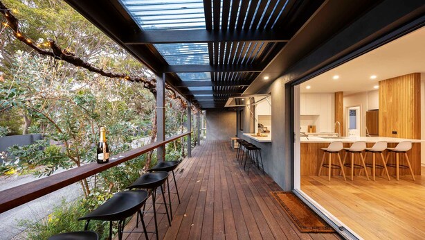 A modern outdoor bar area with wooden flooring, a glass railing, and a view of the garden. - Galene Getaway Walk to Beach Pool Fire (Mount Martha)