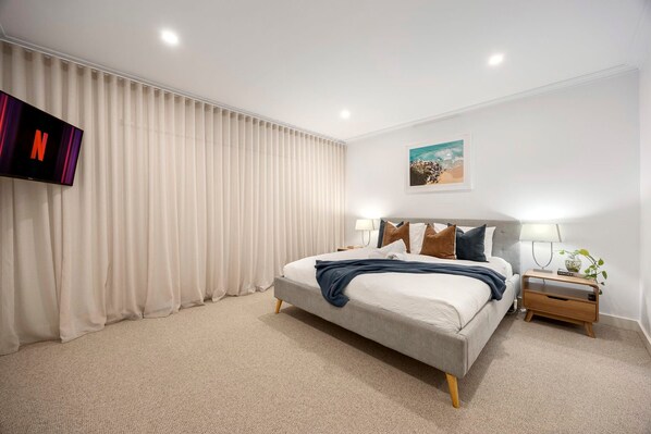 A modern hotel room with a large bed, a flat-screen TV, a bedside table with a lamp, and a painting on the wall. - Galene Getaway Walk to Beach Pool Fire (Mount Martha)