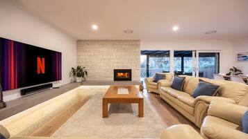 A modern living room with a large flat-screen TV, a stone fireplace, a beige sofa, and a wooden coffee table.