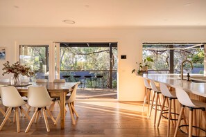 A modern kitchen with a wooden dining table, white chairs, and a bar area with stools. - Galene Getaway Walk to Beach Pool Fire (Mount Martha)