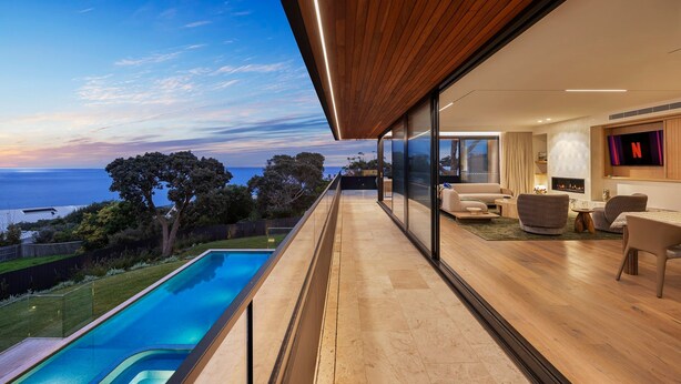 Een modern balkon met een zwembad, houten vloeren en uitzicht op zee.