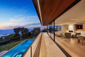 A modern balcony with a pool, wooden flooring, and a view of the sea. - Blanc de Noir Luxe Grandeur Heated Pool and Spa (Mount Martha)
