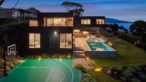 Een modern huis met twee verdiepingen, met een basketbalveld, een zwembad en uitzicht op het water.