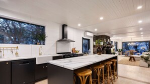 A modern kitchen with a large island, bar stools, and a view of the outdoors through a window. - Bella s Cottage Spa Sauna Large Groups (Yarra Glen)