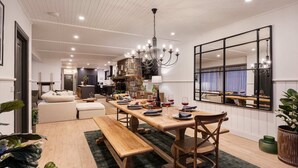 A modern dining area with a wooden table set for a meal, a chandelier, and a large mirror on the wall. - Bella s Cottage Spa Sauna Large Groups (Yarra Glen)