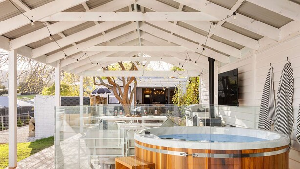 A covered outdoor area with a hot tub, wooden seating, and a glass enclosure. - Bella s Cottage Spa Sauna Large Groups (Yarra Glen)