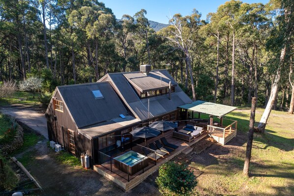 A wooden cabin with a hot tub, outdoor seating, and a deck overlooking a forested area.