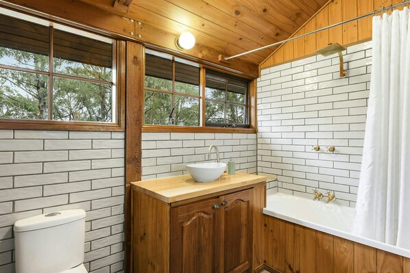 A bathroom with a wooden vanity, a white sink, a bathtub, and a shower.
