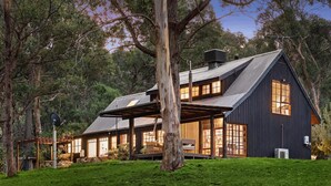 A large, dark wooden house with a sloped roof, surrounded by lush greenery and trees. - Onyx Retreat Healesville Luxury Lodge x Hot Tub (Healesville)