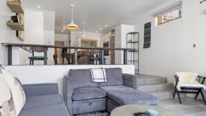 Un salon moderne avec un canapé d’angle gris, une table basse ronde et un escalier menant à un niveau supérieur.