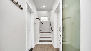 Un couloir étroit avec un plancher en bois, des murs blancs et une porte de douche en verre.