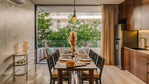 Een eetruimte met een tafel voor zes personen, een moderne keuken met een roestvrijstalen koelkast, en uitzicht op groen via een glazen deur.