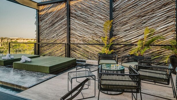Een dakterras met een rieten muur, groene zitplaatsen en zwart rieten meubilair.