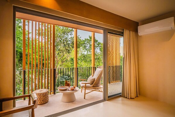 A balcony with a view of greenery, a chair, a table with a bowl, and a potted plant.