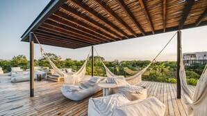 Une terrasse en bois avec des hamacs, des fauteuils en forme de sac et une petite table.