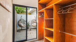 Ein Zimmer mit einer Schiebeglastür, zwei Korbstühlen, einem Holzschrank und einem Metallkleiderständer.