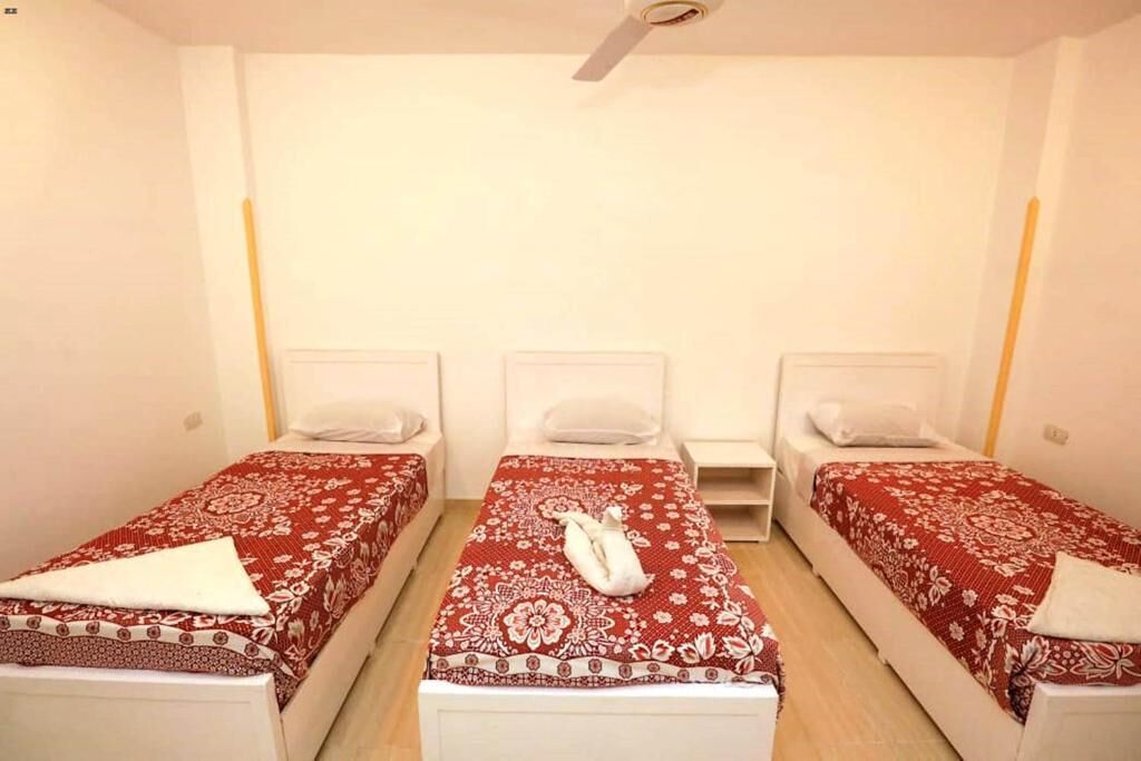 Una habitación con tres camas individuales, cada una con una colcha de cuadros rojos y blancos y almohadas blancas. Hay un ventilador de techo sobre las camas.