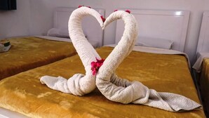 Ein Hotelzimmer mit einem Bett, das mit einer goldenen Decke bedeckt ist, und zwei Handtüchern, die zu einem Herzen geformt sind, mit Blumen.