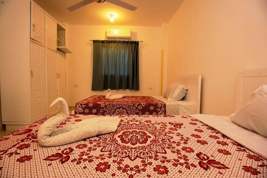 A bedroom with two beds, a ceiling fan, an air conditioning unit, and a window with curtains.