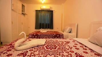 A bedroom with two beds, a ceiling fan, an air conditioning unit, and a window with curtains.