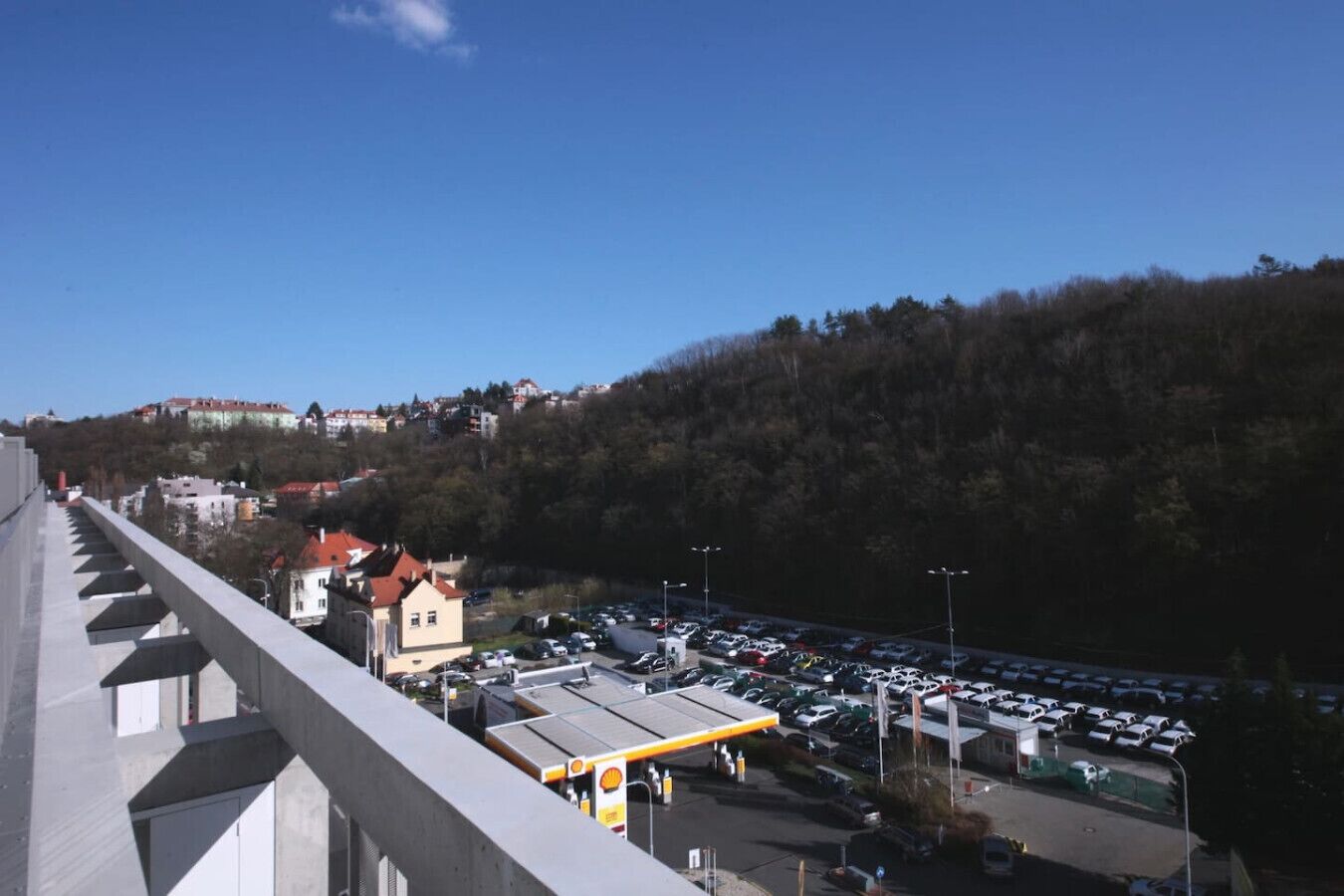 Un parking rempli de voitures, une station-service Shell et des bâtiments en arrière-plan.