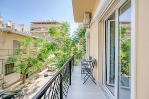 Un balcon avec une table et des chaises, donnant sur une rue bordée d’arbres et sur les immeubles voisins.