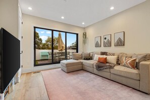 Una sala de estar con un sofá modular, un televisor de pantalla plana y un amplio ventanal corredero que da a un espacio exterior.