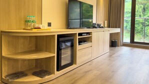 A modern hotel room with a wooden cabinet, a flat-screen TV, a mini-fridge, and a large window offering a view of greenery. - MoonShine Inn (Taoyuan City)