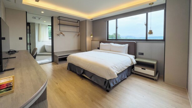 A modern bedroom with a large bed, a desk, and a view of the outdoors through a window. - MoonShine Inn (Taoyuan City)