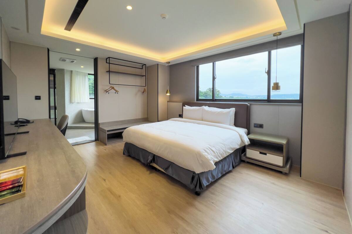 Une chambre moderne avec un grand lit, un bureau et une vue sur l’extérieur par une fenêtre.