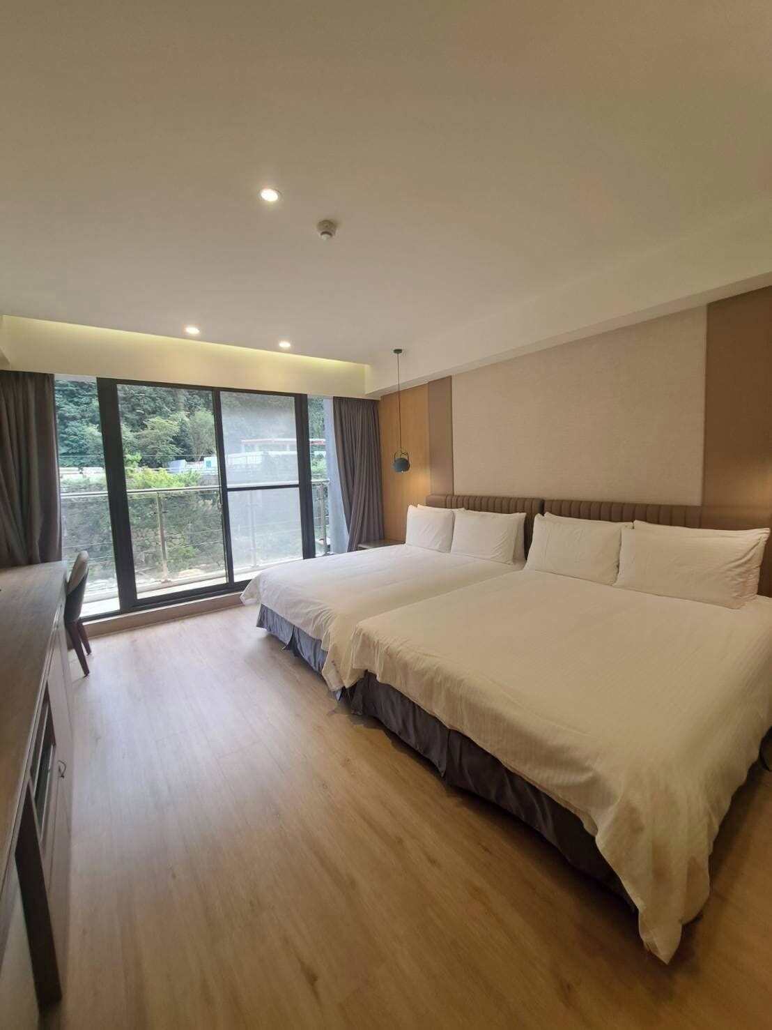 Ein modernes Hotelzimmer mit zwei Betten, einem großen Fenster und Blick auf Grünflächen sowie einem Holzboden.