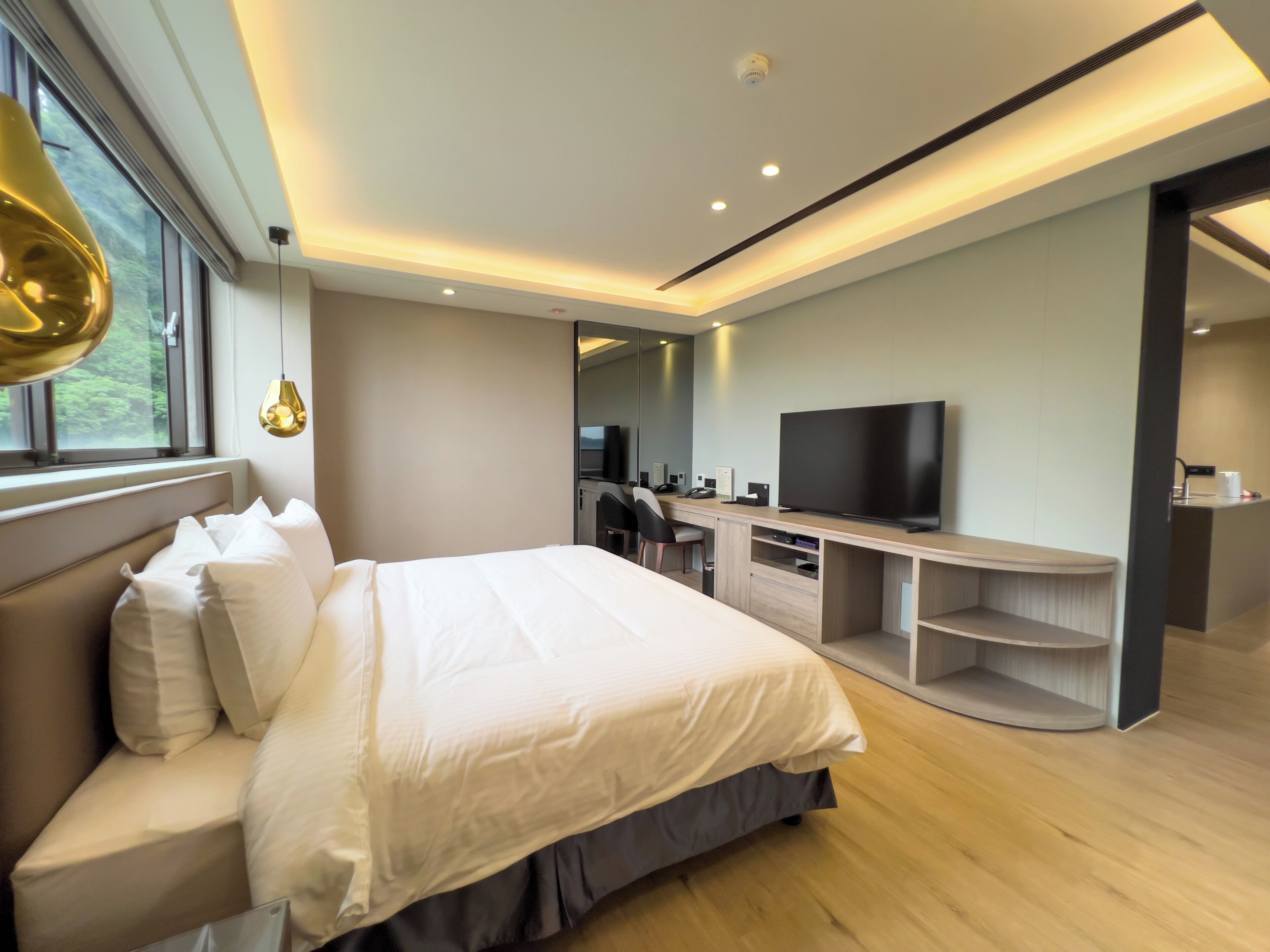 A modern hotel room with a large bed, a desk with a flat-screen TV, and a seating area with a chair.