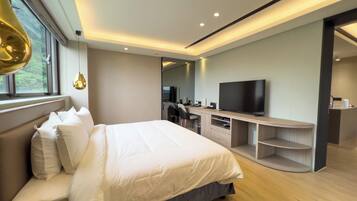 A modern hotel room with a large bed, a desk with a flat-screen TV, and a seating area with a chair.