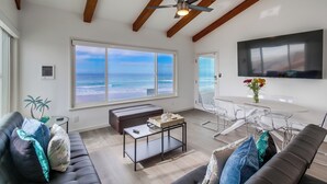 A modern living room with a large window, a ceiling fan, and a flat-screen TV mounted on the wall. - Right on the Famous Mission Beach Boardwalk - Sleeps up to 10 - Best location in Mission Beach (San Diego)