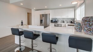 A modern kitchen with a central island, bar stools, stainless steel appliances, and a unique decorative vase. - Right on the Famous Mission Beach Boardwalk - Sleeps up to 10 - Best location in Mission Beach (San Diego)