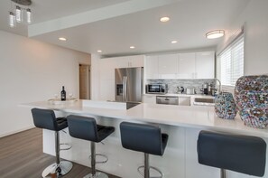 A modern kitchen with a central island, bar stools, stainless steel appliances, and a unique decorative vase. - Right on the Famous Mission Beach Boardwalk - Sleeps up to 10 - Best location in Mission Beach (San Diego)