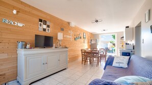 A room with a wooden wall, a white cabinet, a TV, a dining table with chairs, and a bed with pillows. - Natural lagoon and relaxation for 6 (Saint-Vincent-sur-Jard)