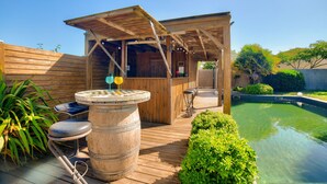A wooden outdoor bar area with a pool, bar stools, and a wooden fence. - Natural lagoon and relaxation for 6 (Saint-Vincent-sur-Jard)