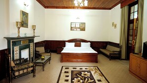 A bedroom with a large bed, a wooden headboard, a sofa, a small table, and a decorative rug. - The Edgeworth (Shimla)