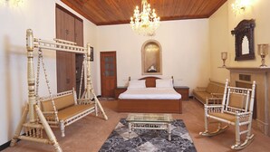 A bedroom with a wooden ceiling, a chandelier, a bed, a rocking chair, a sofa, and a glass coffee table. - The Edgeworth (Shimla)
