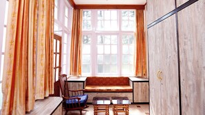 A room with a wooden bench, a chair, and a small table near a large window with curtains. - The Edgeworth (Shimla)