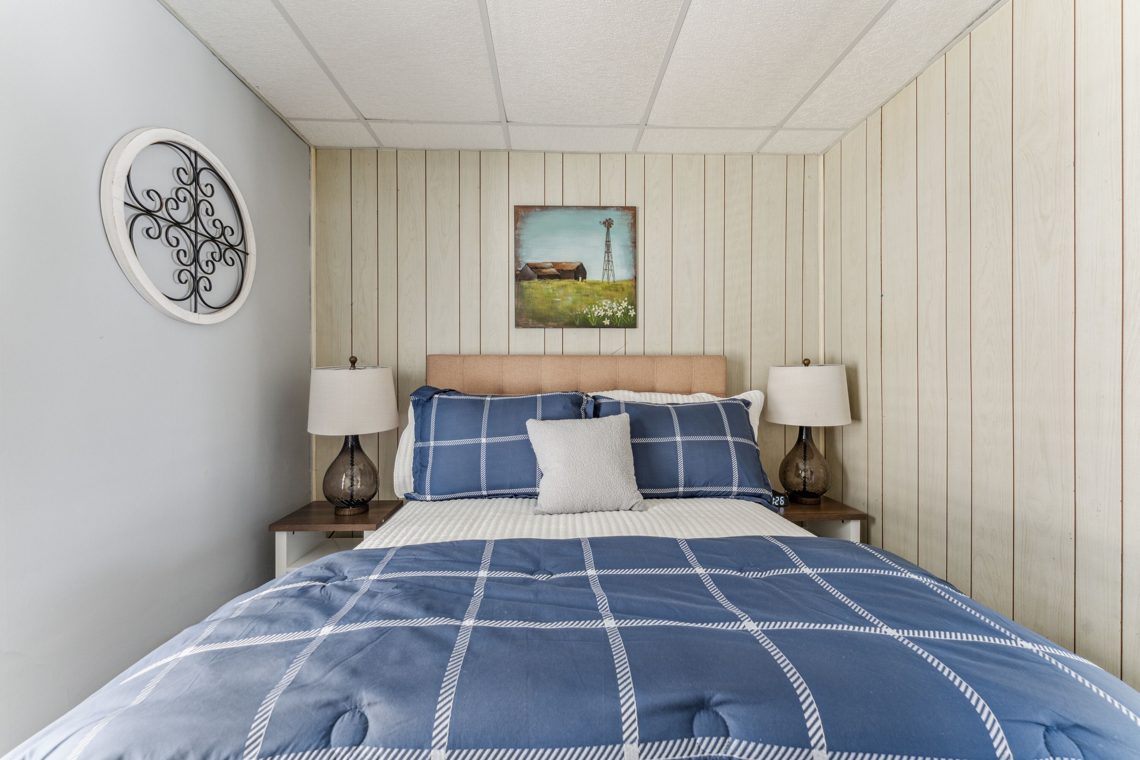 A bedroom with a bed, two bedside lamps, a wall-mounted painting, and a decorative wall piece.
