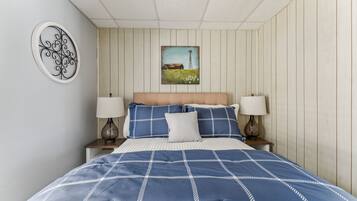 A bedroom with a bed, two bedside lamps, a wall-mounted painting, and a decorative wall piece.
