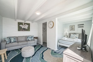 A modern, well-lit room with a grey sofa, a patterned rug, a wooden desk, and a bed with a striped bedspread. - Beautiful Lake View Retreat Drivable To Theme Parks 3 Bedroom Home (Haines City)